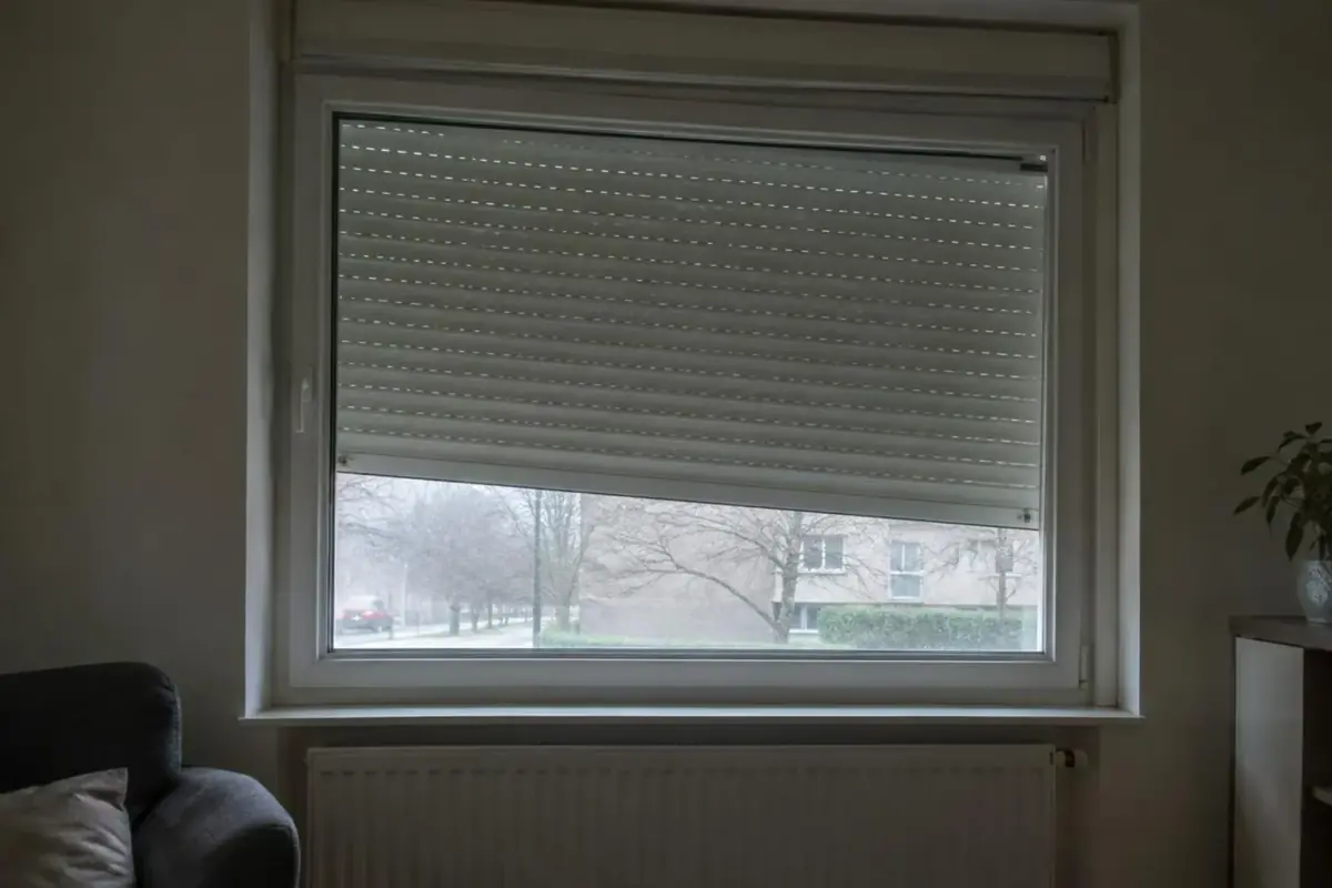 Volet roulant en PVC blanc resté coincé de biais à mi-hauteur d'une fenêtre de salon